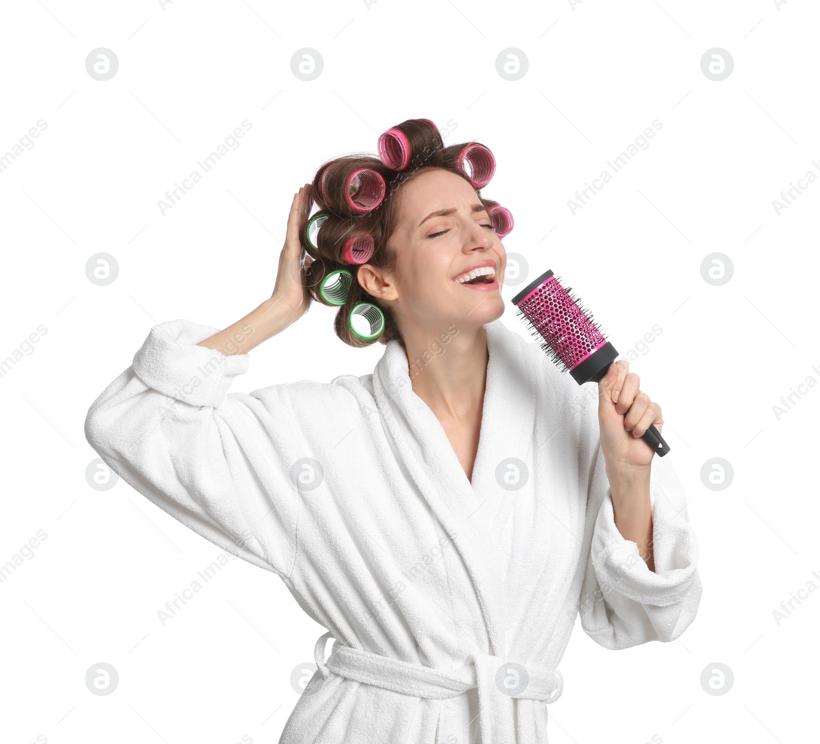 Photo of Beautiful young woman in bathrobe with hair curlers singing into hairbrush on white background