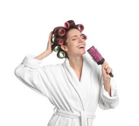 Beautiful young woman in bathrobe with hair curlers singing into hairbrush on white background