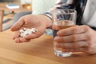 Man holding many pills and glass of water at table, closeup