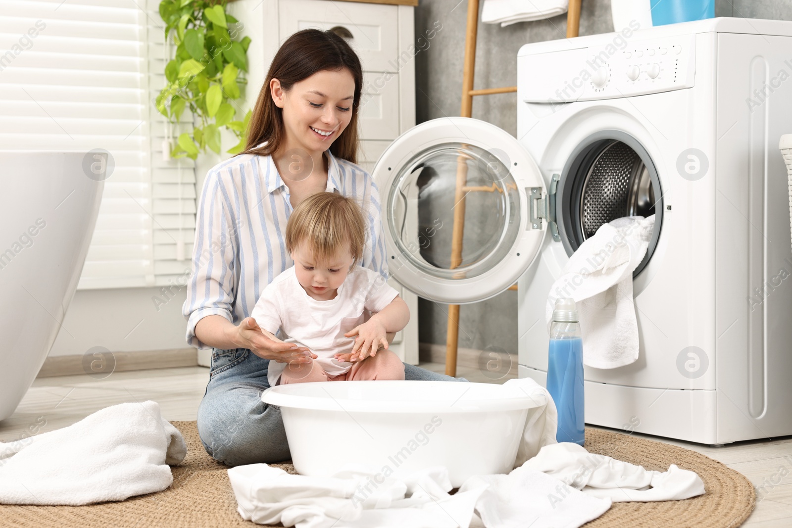 Photo of Happy mother with her daughter having fun while washing baby clothes in bathroom