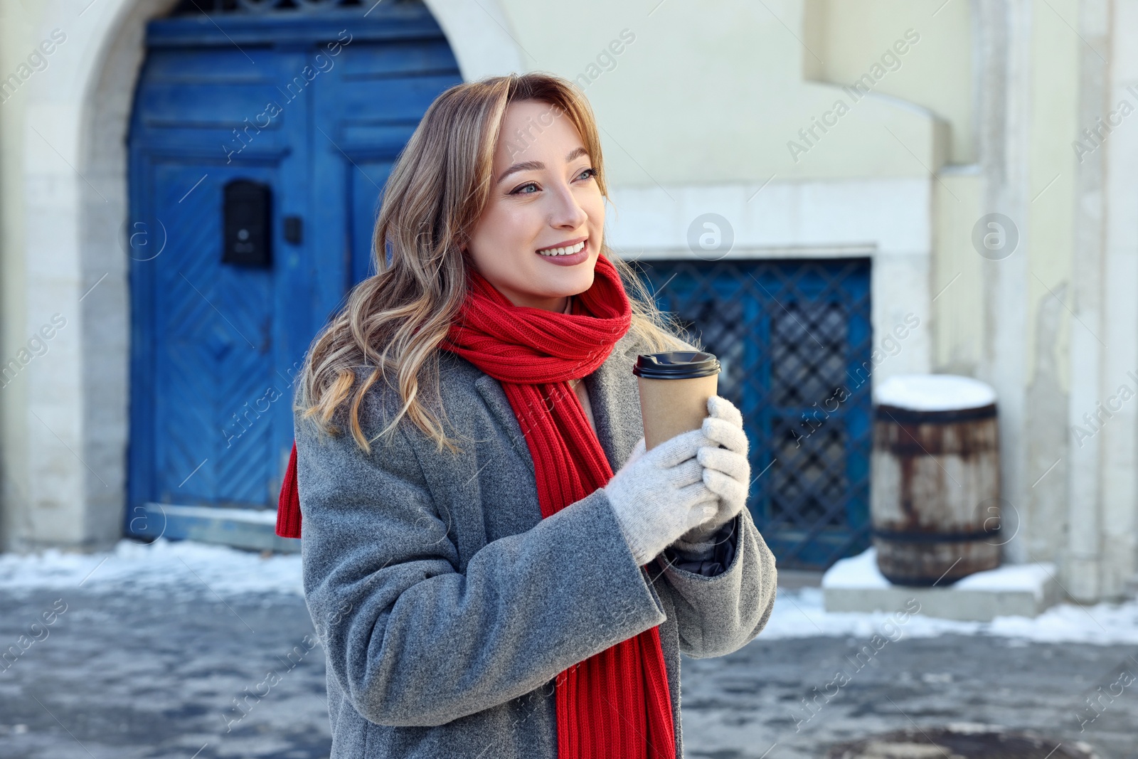 Photo of Portrait of smiling woman with paper cup of coffee on city street in winter