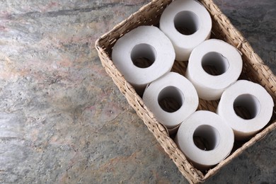 Photo of Toilet paper rolls in wicker basket on textured table, top view. Space for text