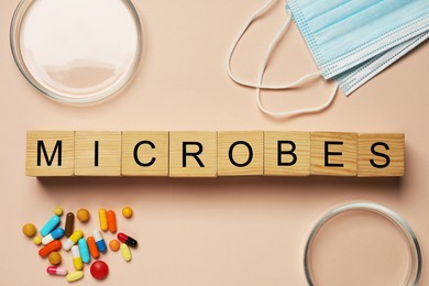 Photo of Word Microbes made with wooden cubes, colorful pills, Petri dishes and face masks on beige background, flat lay