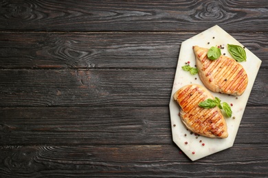 Photo of Tasty grilled chicken fillets with peppercorns and green basil on black wooden table, top view. Space for text