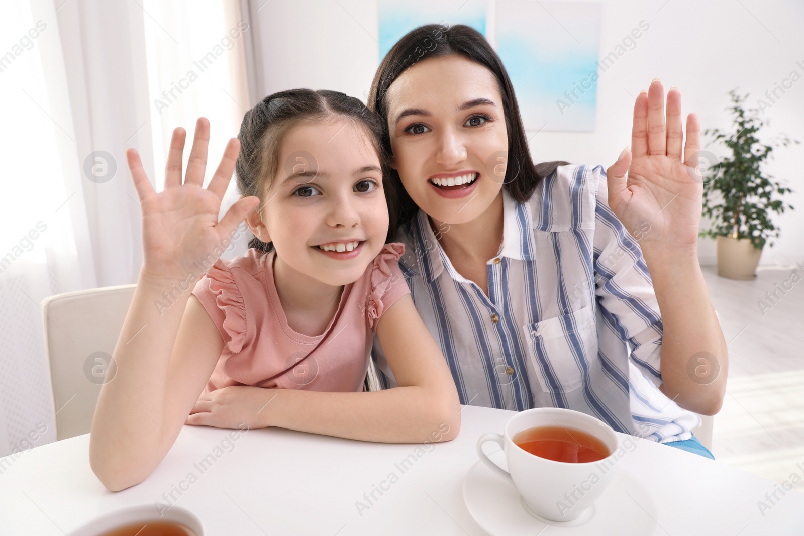 Photo of Mother and daughter using video chat at table indoors, view from camera perspective