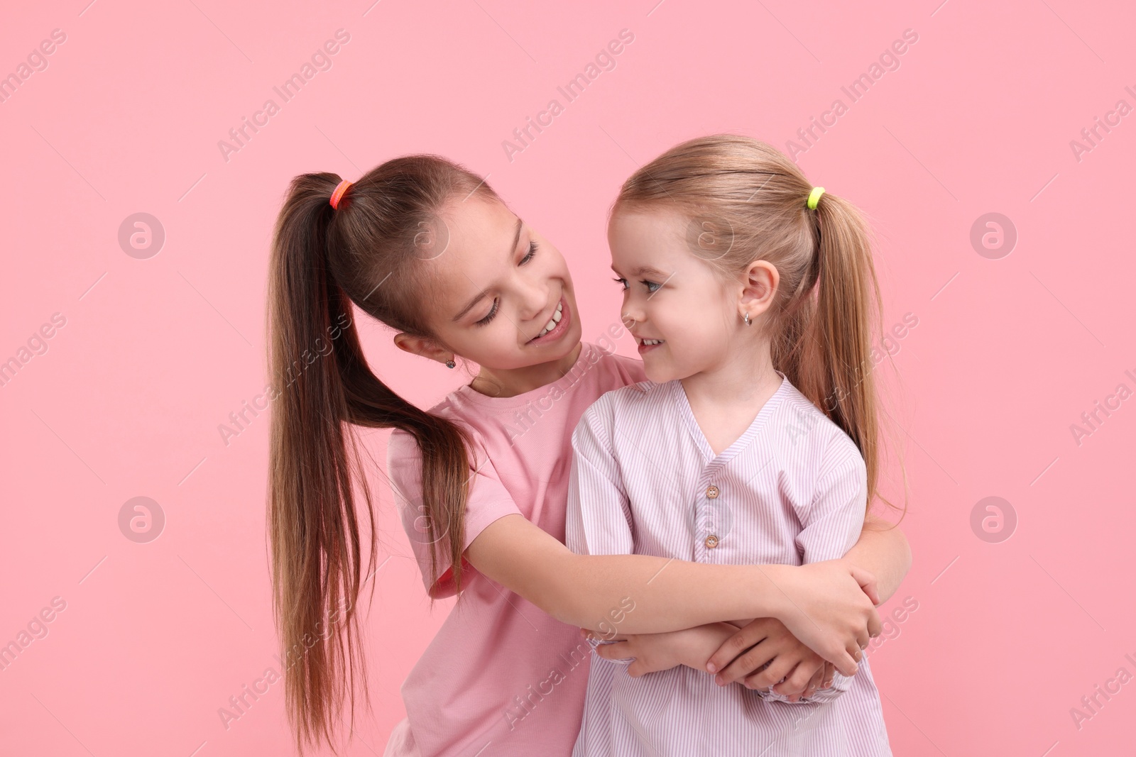 Photo of Portrait of cute little sisters on pink background