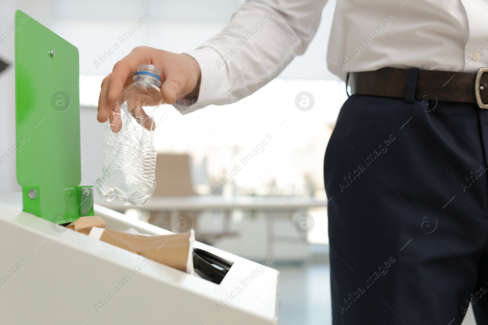 Photo of Man putting used plastic bottle into trash bin in office, closeup. Waste recycling