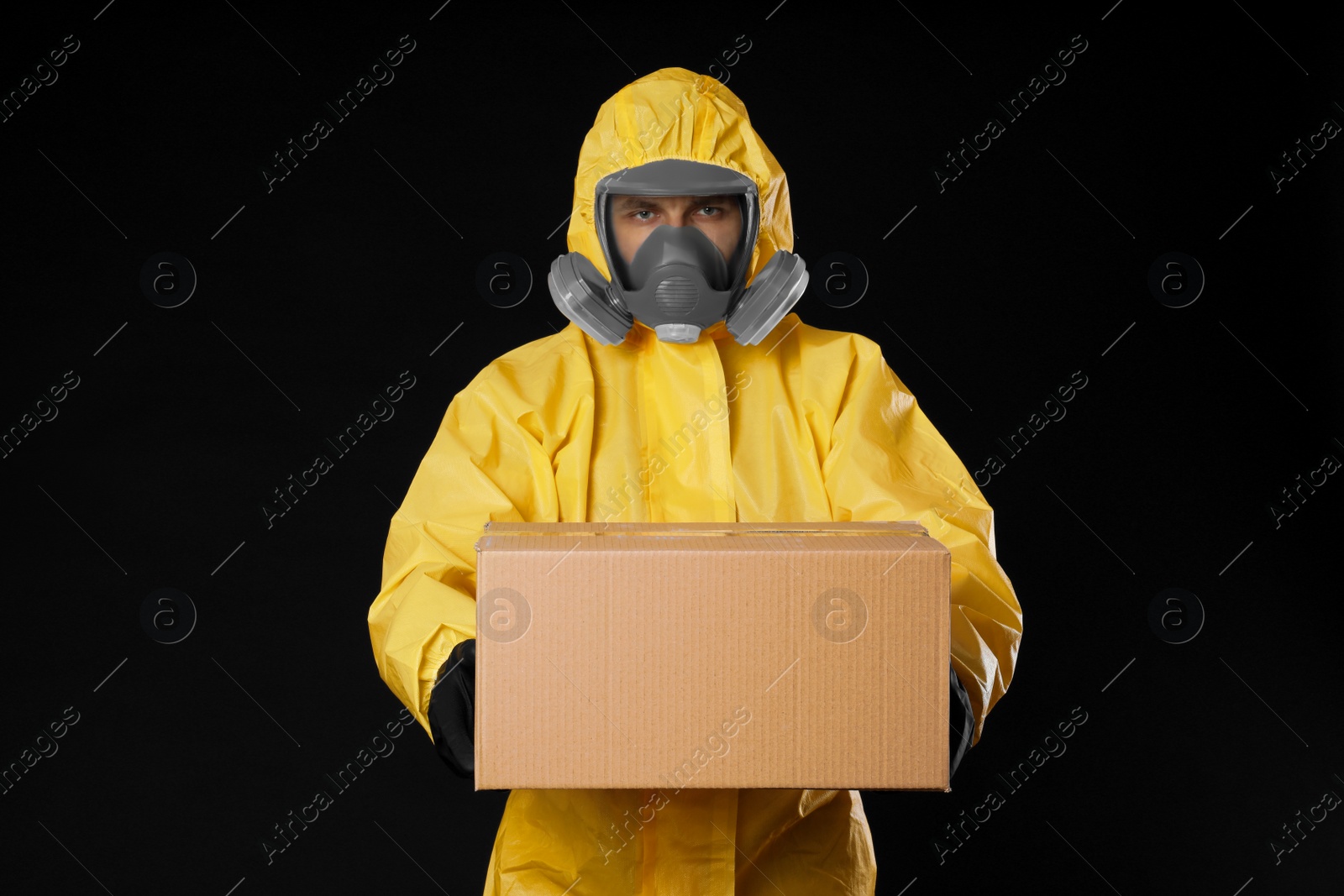 Photo of Man wearing chemical protective suit with cardboard box on black background. Prevention of virus spread