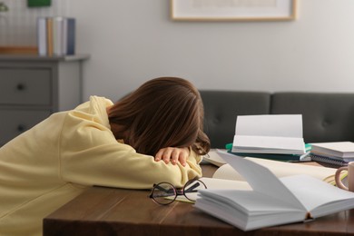 Photo of Young tired woman sleeping near books at wooden table in room