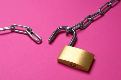 Steel padlock and chain on pink background, closeup