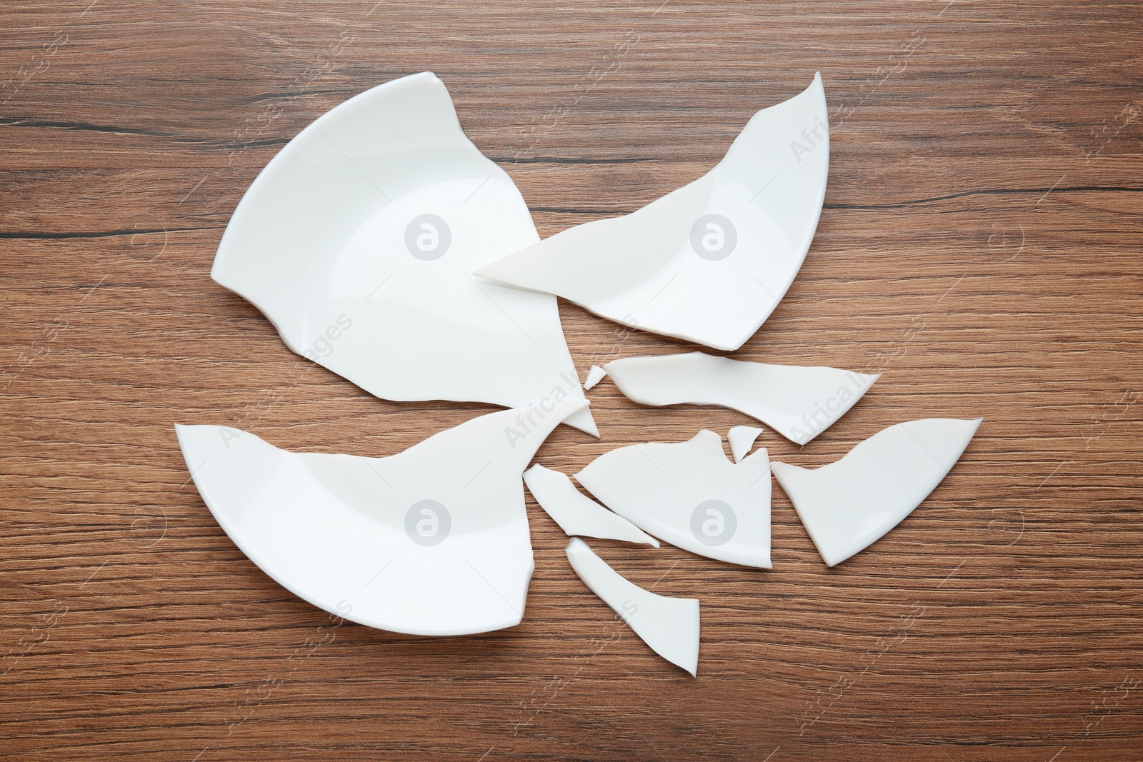 Photo of Pieces of broken ceramic plate on wooden table, flat lay