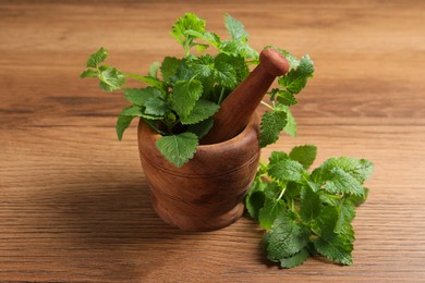 Photo of Mortar with pestle and fresh lemon balm on wooden table