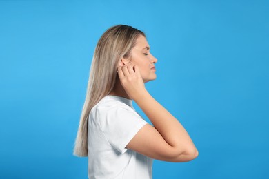 Young woman cleaning ear with cotton swab on light blue background