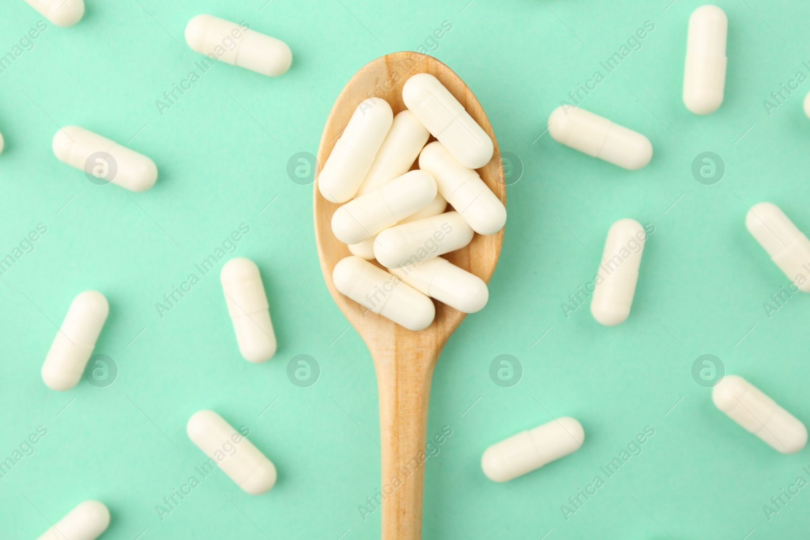 Photo of Wooden spoon with vitamin capsules on turquoise background, flat lay