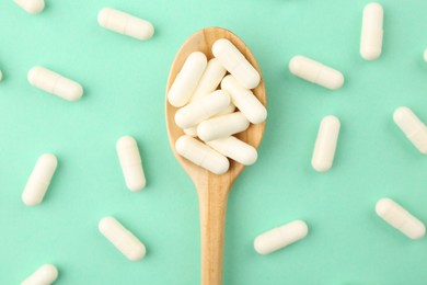 Photo of Wooden spoon with vitamin capsules on turquoise background, flat lay
