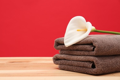 Soft clean towels with beautiful flower on table against color background. Space for text