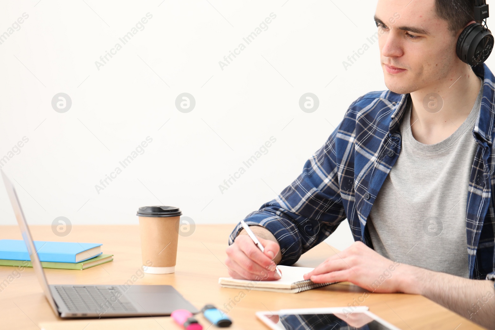 Photo of E-learning. Young man taking notes during online lesson at table indoors.