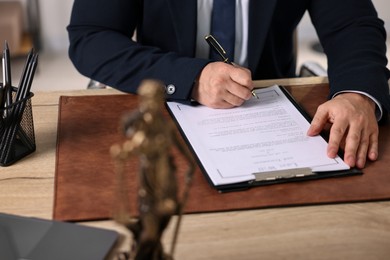 Notary writing notes at wooden table in office, closeup