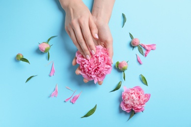 Woman holding beautiful peony flower on color background, top view