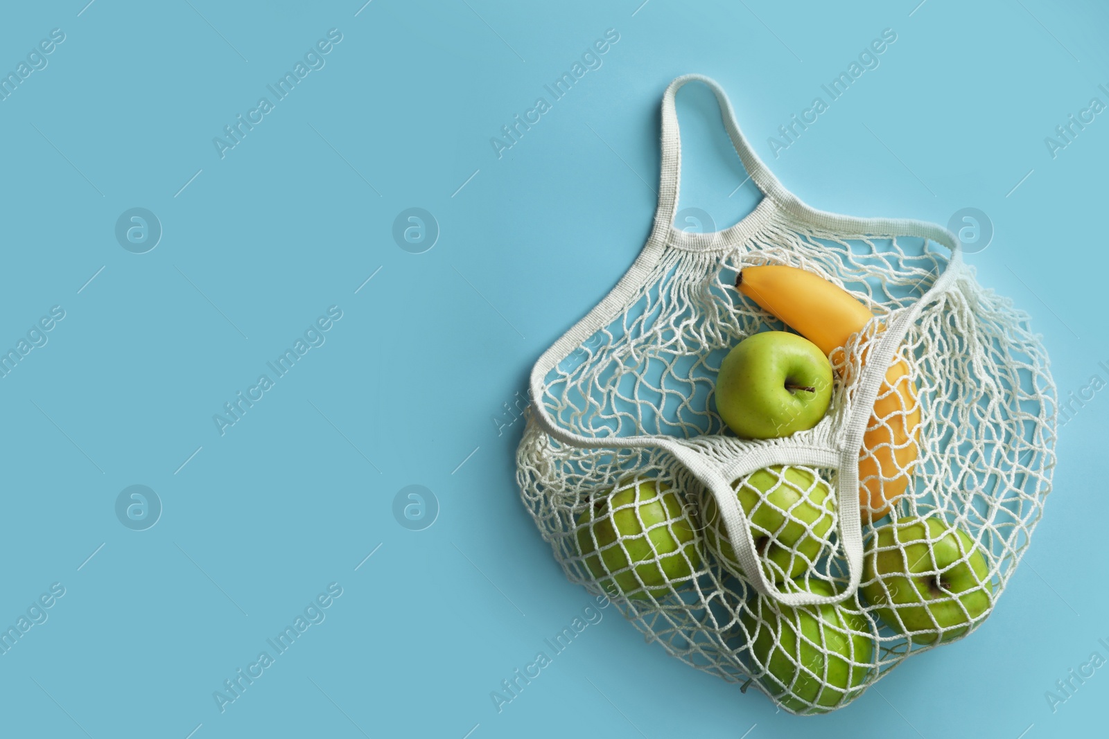 Photo of Net bag with fruits on light blue background, top view. Space for text