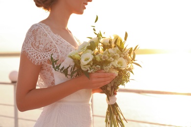 Photo of Bride in beautiful wedding dress with bouquet near river on sunset, closeup