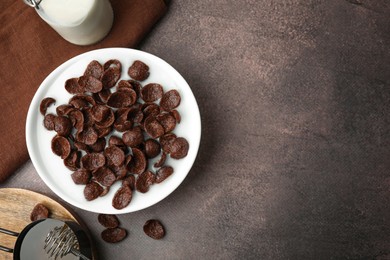 Photo of Breakfast cereal. Chocolate corn flakes and milk in bowl on brown table, flat lay. Space for text