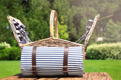 Photo of Picnic basket with blanket on wooden table in garden