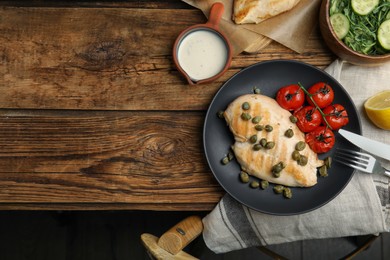Photo of Delicious cooked chicken fillet with capers and tomatoes served on wooden table, flat lay. Space for text