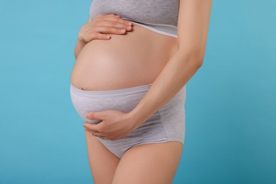 Pregnant woman in comfortable maternity underwear on light blue background, closeup