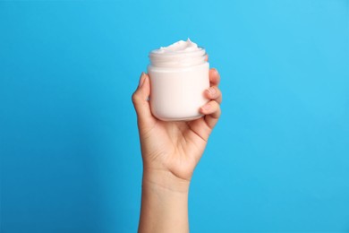 Photo of Woman holding jar of face cream on light blue background, closeup