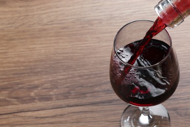 Photo of Pouring tasty red wine in glass at wooden table, closeup. Space for text