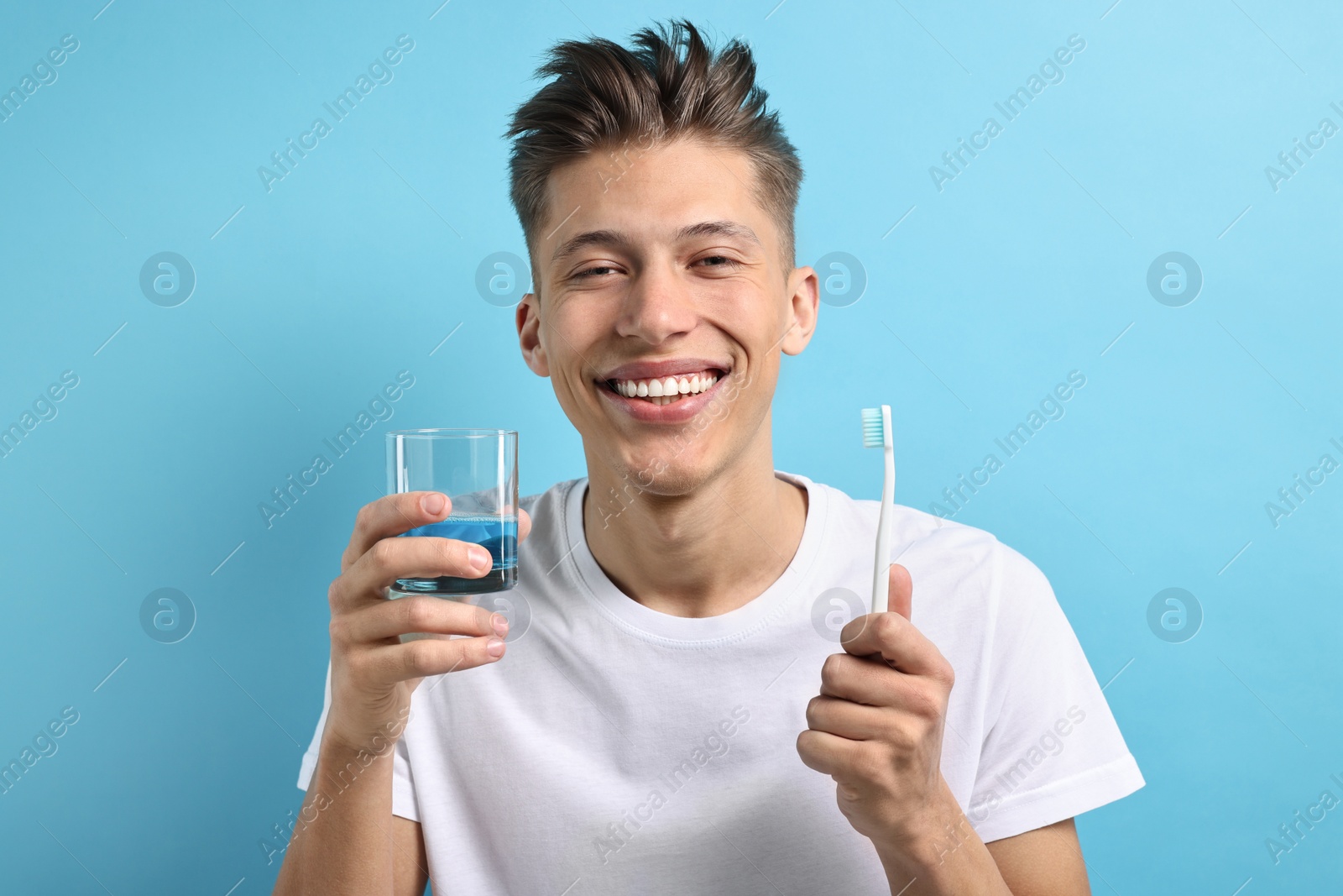 Photo of Young man with mouthwash and toothbrush on light blue background