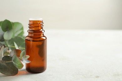 Bottle of eucalyptus essential oil and leaves on white table. Space for text