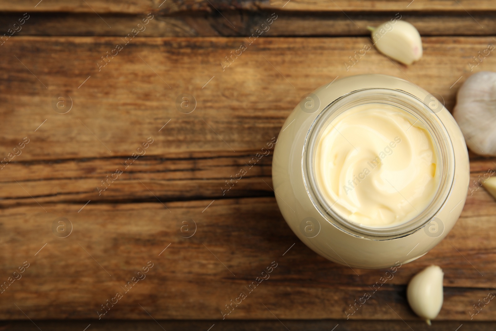 Photo of Jar of delicious mayonnaise and fresh garlic on wooden table, flat lay. Space for text