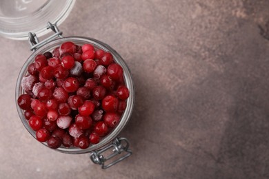 Photo of Frozen red cranberries in glass jar on brown textured table, top view. Space for text