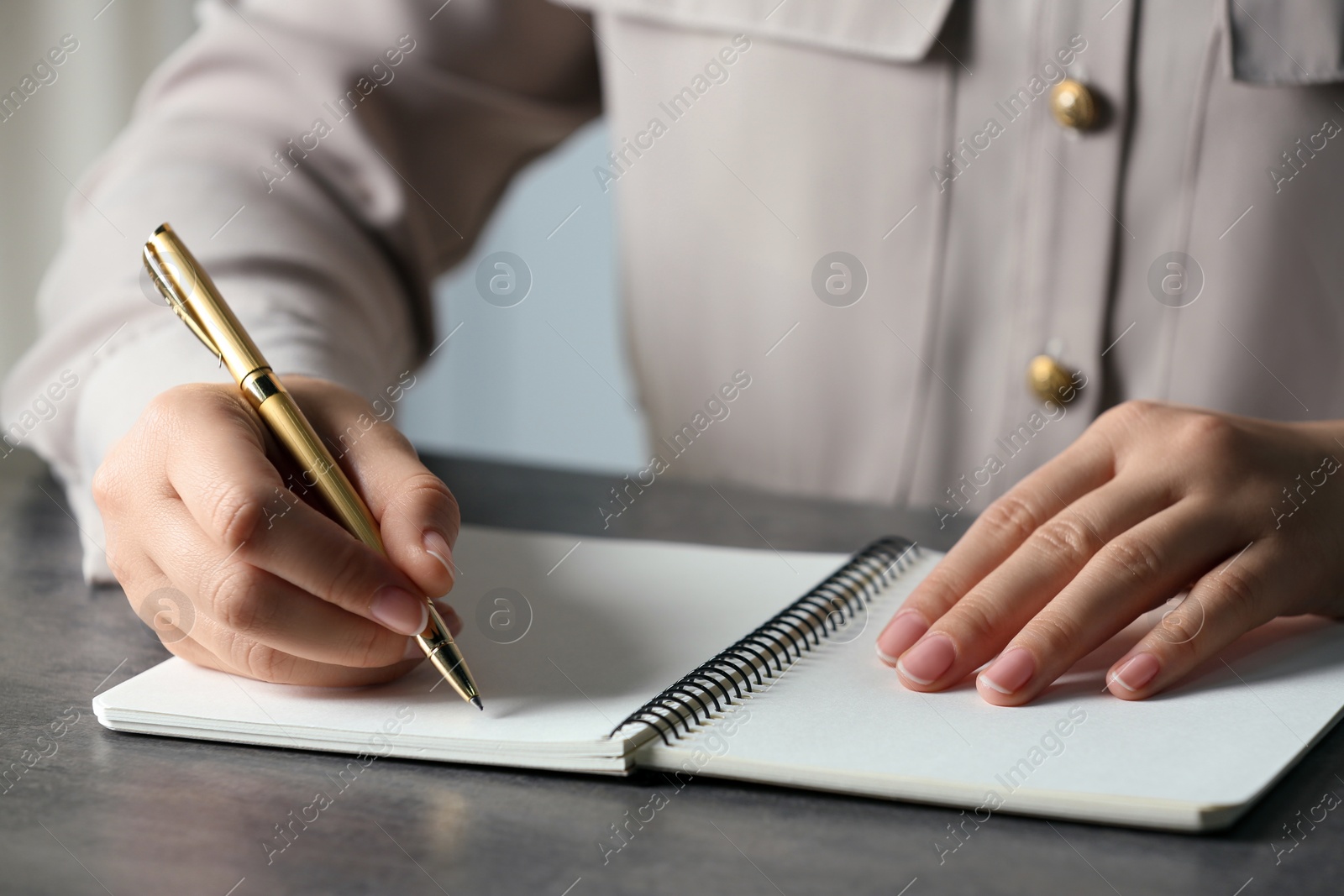 Photo of Woman writing in notebook with pen at grey table, closeup