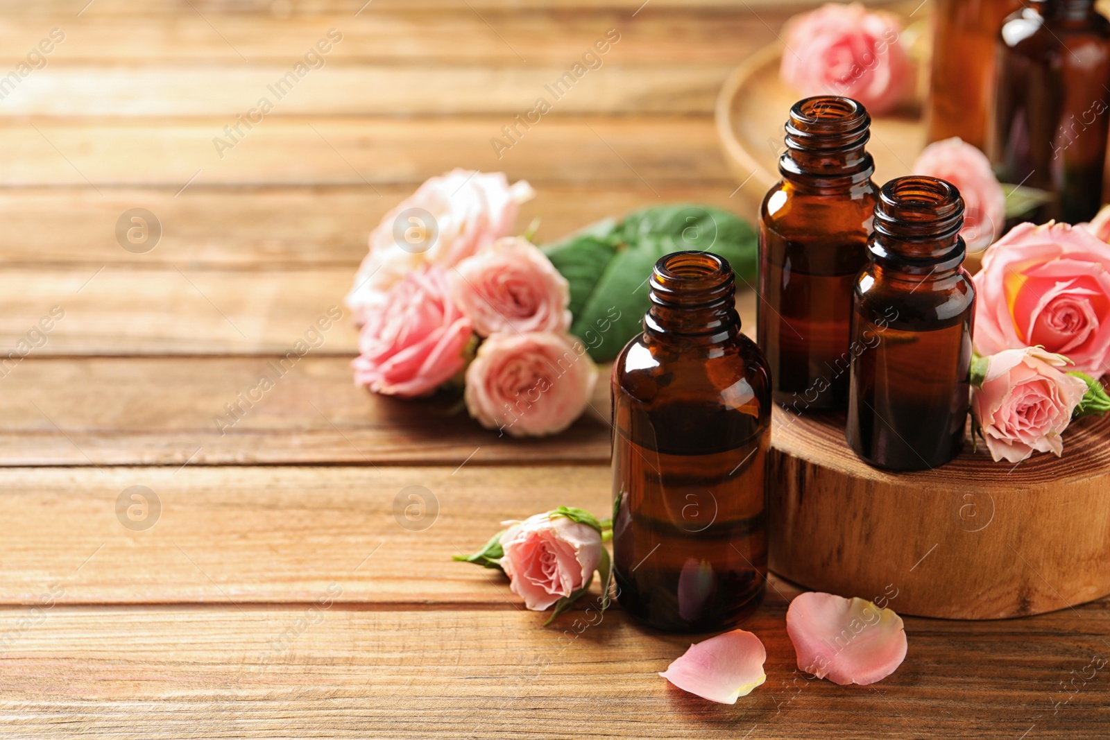 Photo of Bottles of rose essential oil and fresh flowers on wooden table, space for text