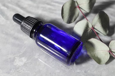 Photo of Bottle of face serum and leaves in water on light background, closeup