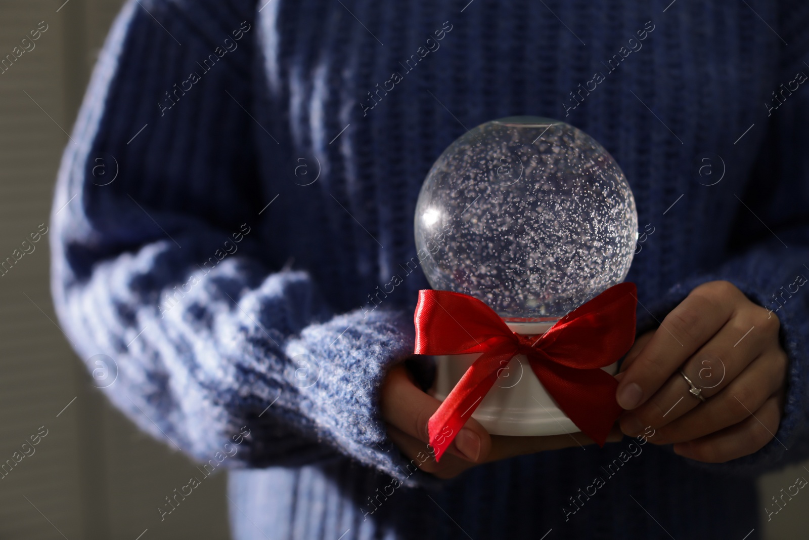 Photo of Woman holding Christmas snow globe with red bow, closeup. Space for text