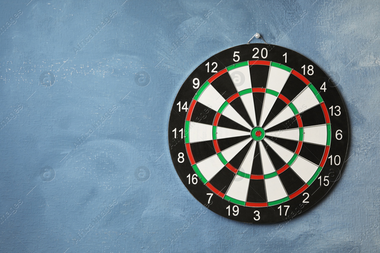 Photo of Dart board hanging on blue textured wall. Space for text