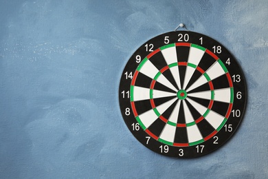 Dart board hanging on blue textured wall. Space for text