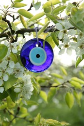 Evil eye amulet hanging on blossoming spring tree outdoors, closeup