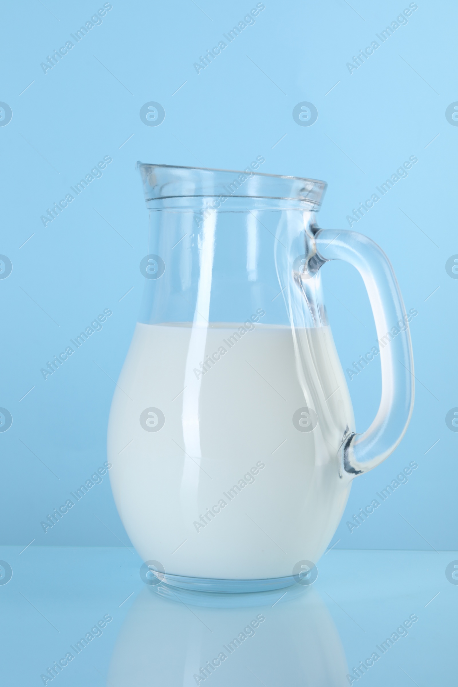 Photo of Jug of fresh milk on light blue background