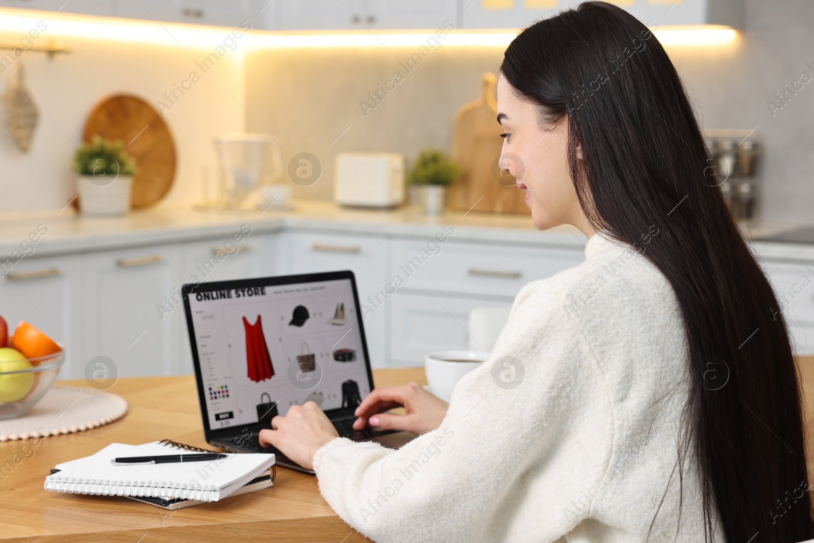 Photo of Young woman with laptop shopping online at wooden table in kitchen