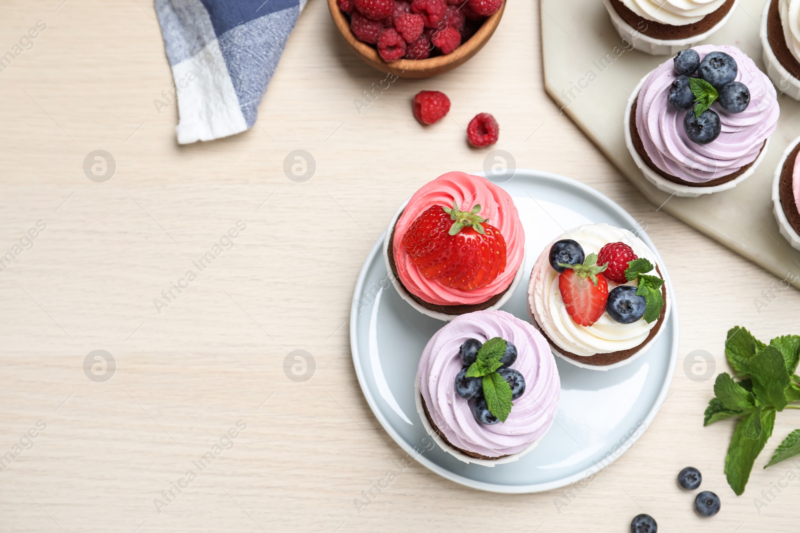 Photo of Sweet cupcakes with fresh berries on light wooden table, flat lay. Space for text