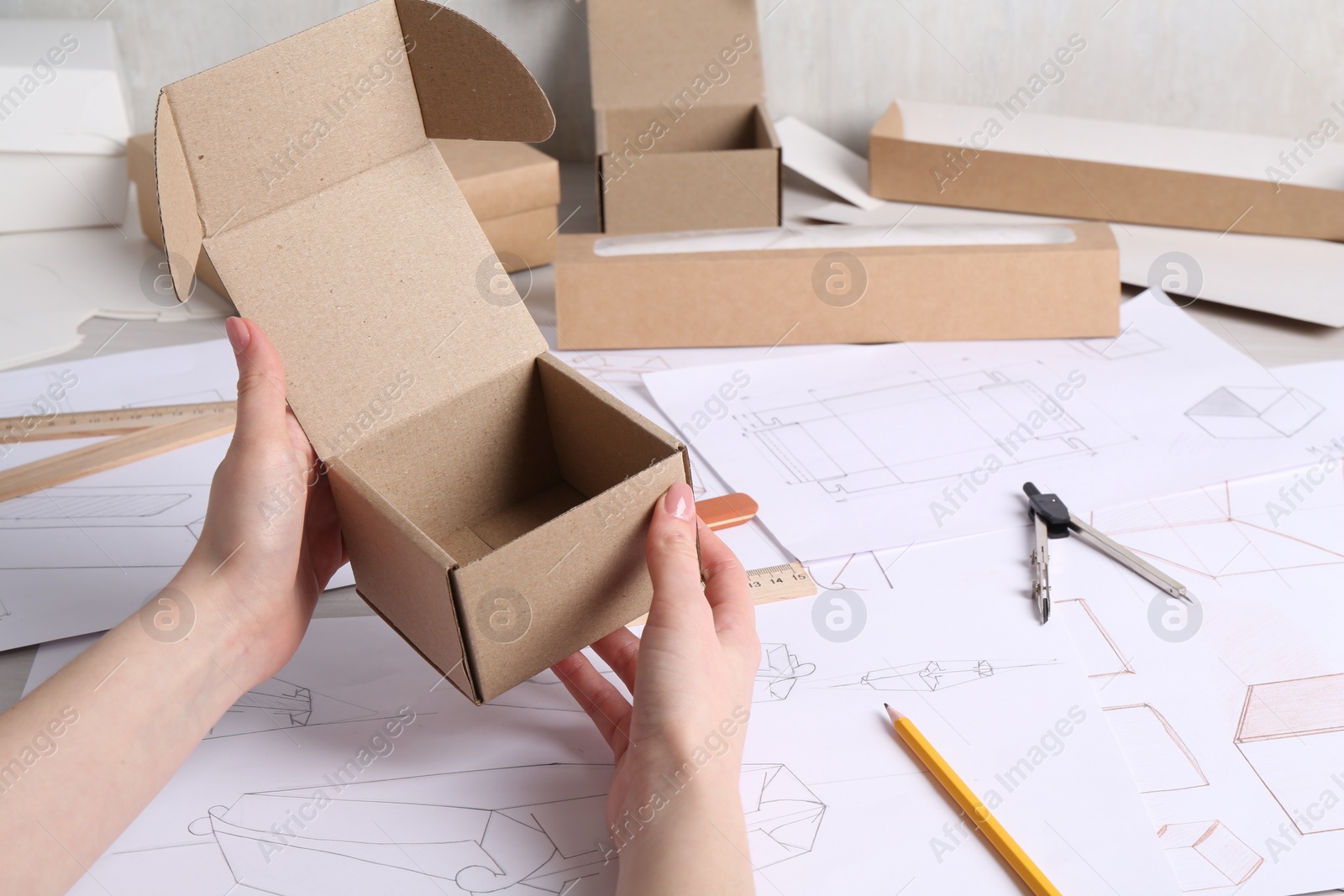 Photo of Woman holding cardboard box near drawings at table, closeup