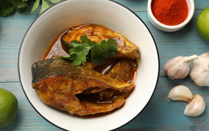 Photo of Tasty fish curry and ingredients on light blue wooden table, flat lay. Indian cuisine