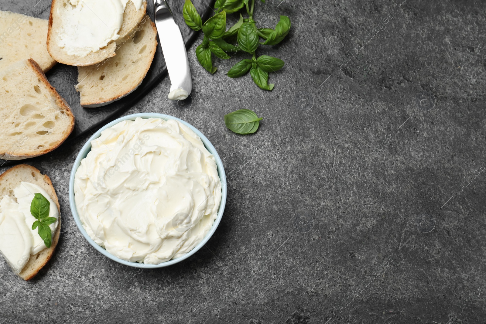 Photo of Tasty cream cheese, fresh bread and basil on grey table, flat lay. Space for text