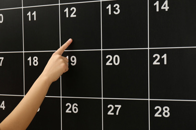 Woman pointing on date of board calendar, closeup