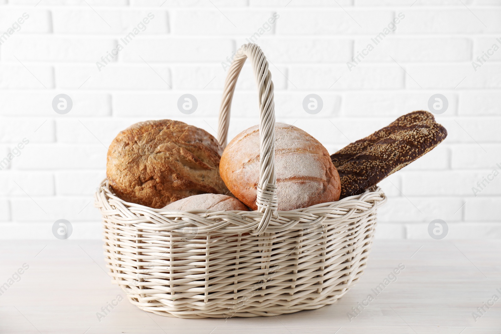 Photo of Different types of bread in wicker basket on white wooden table